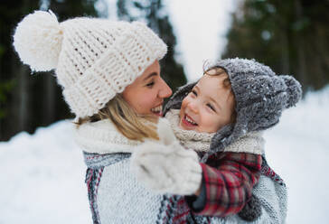 Seitenansicht einer fröhlichen Mutter mit ihrer kleinen Tochter, die lachend in der winterlichen Natur steht. - HPIF13365