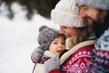 Seitenansicht von Vater und Mutter mit Kleinkind in winterlicher Natur, stehend im Schnee. - HPIF13370