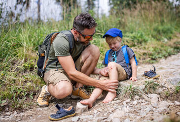 Vater mit verärgerten kleinen Sohn auf Wanderung im Freien im Sommer Natur, fallen und zerkratzt Knie Konzept. - HPIF13388