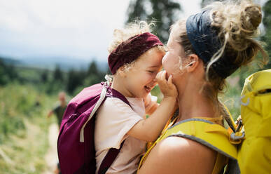Fröhliche Mutter mit kleiner Tochter beim Wandern in der sommerlichen Natur, kuschelnd. - HPIF13394