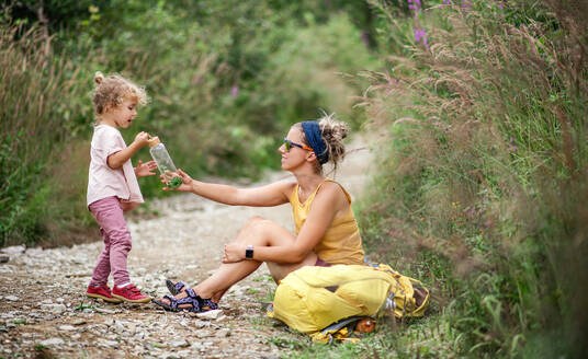 Mutter mit kleinem Kleinkind Tochter Wandern im Freien im Sommer Natur, Ausruhen und Trinken von Wasser. - HPIF13401