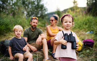 Vorderansicht einer Familie mit kleinen Kindern, die in der sommerlichen Natur wandern, sitzen und sich ausruhen. - HPIF13412