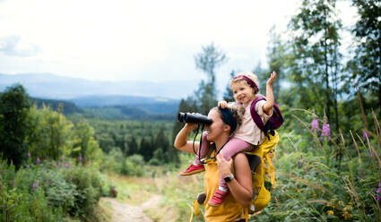 Seitenansicht einer Mutter mit ihrer kleinen Tochter, die im Sommer in der Natur wandert und ein Fernglas benutzt. - HPIF13414
