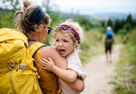 Rear view of mother with small crying toddler daughter hiking outdoors in summer nature. - HPIF13422