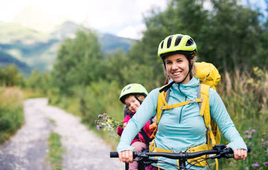 Portrait of mother with small daughter cycling outdoors in summer nature, looking at camera. - HPIF13429