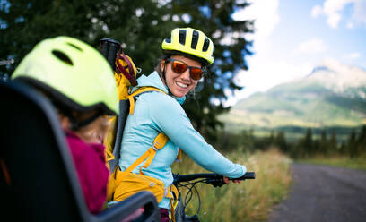 Portrait of mother with small daughter cycling outdoors in summer nature, looking at camera. - HPIF13439