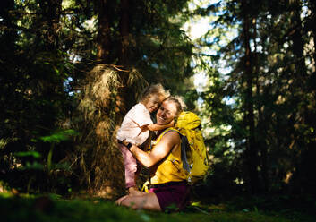 Seitenansicht einer glücklichen Mutter mit ihrer kleinen Tochter in der sommerlichen Natur, die sich umarmen und ausruhen. - HPIF13463