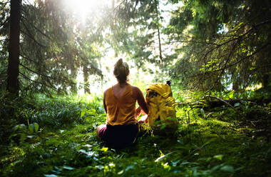 Rear view of woman hiker sitting on the ground outdoors in forest, resting and meditating. - HPIF13464