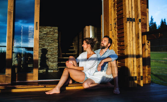 Portrait of happy couple sitting on patio of wooden cabin, holiday in nature concept. - HPIF13470