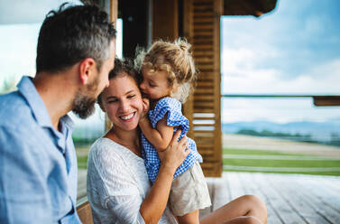 Happy family with small daughter sitting on patio of wooden cabin, holiday in nature concept. - HPIF13471