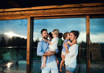 Happy family with small children standing on patio by wooden cabin, holiday in nature concept. - HPIF13475