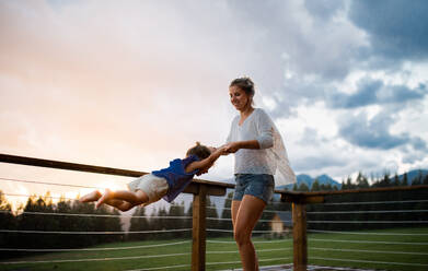 Glückliche Mutter mit kleiner Tochter, die auf der Veranda einer Holzhütte spielt, Urlaub in der Natur Konzept. - HPIF13477