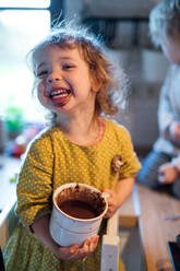 Happy small girl with dirty mouth indoors in kitchen at home, eating pudding. - HPIF13483