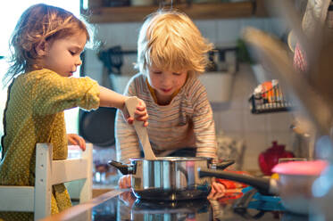 Glücklicher kleiner Junge und Mädchen drinnen in der Küche zu Hause, die beim Kochen helfen. - HPIF13484