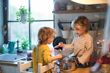 Glücklicher kleiner Junge und Mädchen drinnen in der Küche zu Hause, die beim Kochen helfen. - HPIF13487