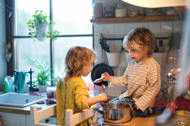 Happy small boy and girl indoors in kitchen at home, helping with cooking. - HPIF13487