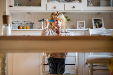 Sad small boy with dirty mouth indoors in kitchen at home, eating pudding. - HPIF13492