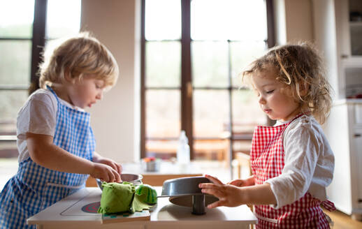 Glücklicher kleiner Junge und Mädchen mit Schürze spielen drinnen mit Spielzeug Küche zu Hause. - HPIF13500