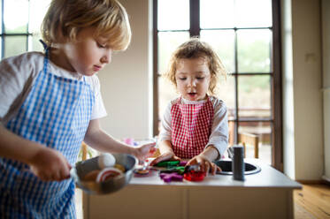 Happy small boy and girl with apron playing indoors with toy kitchen at home. - HPIF13501