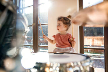 Portrait of happy small girl indoors at home, playing drums. - HPIF13508