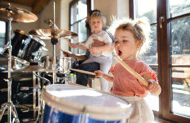 Portrait of happy small girl indoors at home, playing drums. - HPIF13511