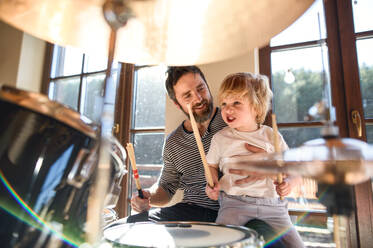Fröhlicher kleiner Junge mit Vater zu Hause, der Schlagzeug spielt. - HPIF13512