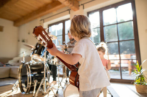 Rückansicht eines kleinen Jungen mit einer Familie in einem Haus, der Gitarre spielt. - HPIF13516