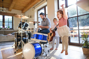 Portrait of happy small children with father indoors at home, playing drums. - HPIF13517