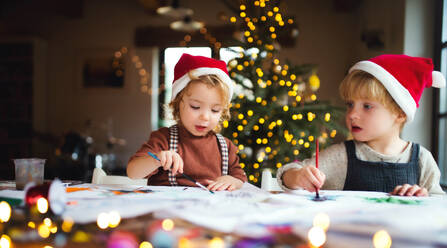 Porträt eines glücklichen kleinen Mädchens und eines Jungen, die zu Weihnachten zu Hause sind und Bilder malen. - HPIF13520