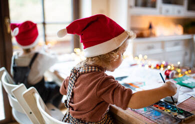 Rückansicht eines glücklichen kleinen Mädchens und eines Jungen, die zu Hause an Weihnachten Bilder malen. - HPIF13526