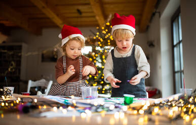 Porträt eines glücklichen kleinen Mädchens und eines Jungen, die sich zu Weihnachten zu Hause mit Kunst und Handwerk beschäftigen. - HPIF13530