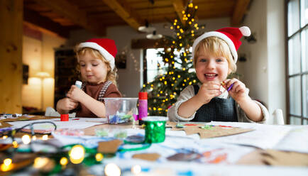 Porträt eines glücklichen kleinen Mädchens und eines Jungen, die sich zu Weihnachten zu Hause mit Kunst und Handwerk beschäftigen. - HPIF13537