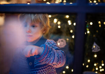 Portrait of happy small boy indoors at home at Christmas, playing by window at night. - HPIF13552