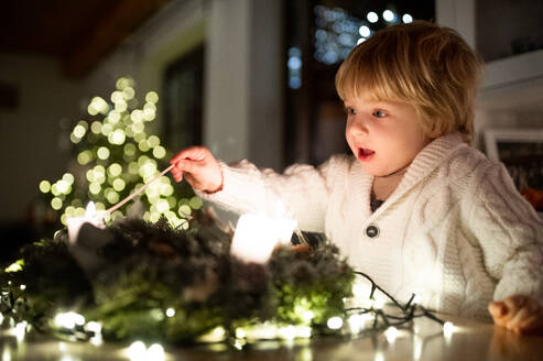 Porträt eines kleinen Jungen, der zu Weihnachten zu Hause ist und Kerzen auf einem Kranz anzündet. - HPIF13555