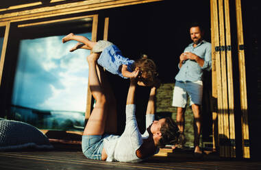 Glückliche Familie mit kleiner Tochter, die sich auf der Terrasse einer Holzhütte amüsiert, Urlaub in der Natur Konzept. - HPIF13559