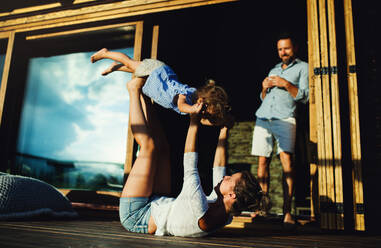 Happy family with small daughter having fun on patio of wooden cabin, holiday in nature concept. - HPIF13559