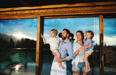 Happy family with small children standing on patio by wooden cabin, holiday in nature concept. - HPIF13563