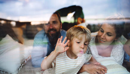 Porträt eines kleinen Jungen mit seinen Eltern am Fenster, Konzept Urlaub in der Natur, Aufnahme durch Glas. - HPIF13568