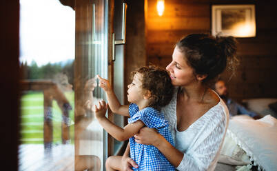 Kleines Mädchen mit Eltern am Fenster in Holzhütte, Urlaub in der Natur Konzept. - HPIF13569