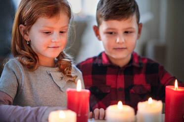 Portrait of small girl and boy indoors at home at Christmas, holding candles. - HPIF13584