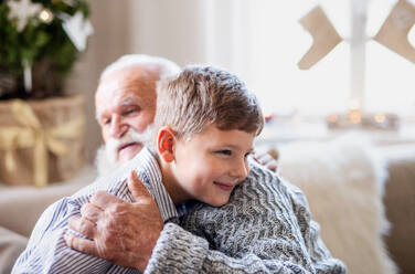 Porträt eines kleinen Jungen mit seinem älteren Großvater, der sich zu Weihnachten zu Hause umarmt. - HPIF13592