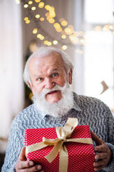 Vorderansicht eines glücklichen älteren Mannes mit einer Geschenkbox zu Hause zu Weihnachten, der in die Kamera schaut. - HPIF13595