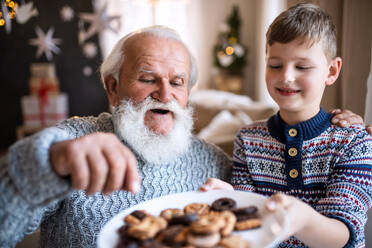 Porträt eines kleinen Jungen mit seinem Großvater, der zu Weihnachten zu Hause ist und Kekse isst. - HPIF13602