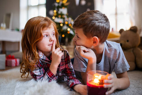 Porträt eines kleinen Mädchens und eines Jungen mit einer Kerze in einem Haus zu Weihnachten, die eine stille Geste machen. - HPIF13604