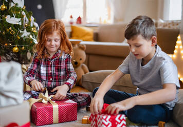 Kleines Mädchen und kleiner Junge im Schlafanzug zu Hause an Weihnachten beim Öffnen der Geschenke am Morgen. - HPIF13607