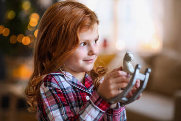 Side view portrait of small girl indoors at home at Christmas, holding wooden horse. - HPIF13612