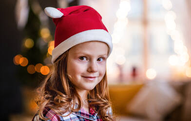 Nahaufnahme eines kleinen Mädchens mit Weihnachtsmannmütze zu Hause, das in eine Kamera schaut. - HPIF13613