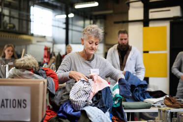 Portrait of volunteers sorting out donated clothes in community charity donation center. - HPIF13618