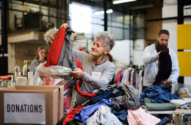 Portrait of volunteers sorting out donated clothes in community charity donation center, coronavirus concept. - HPIF13619