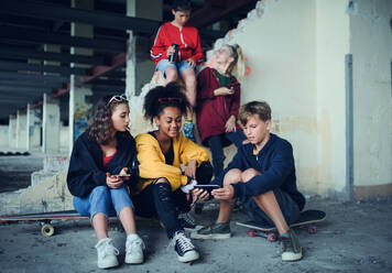 Front view of group of teenagers gang sitting indoors in abandoned building, using smartphones. - HPIF13625